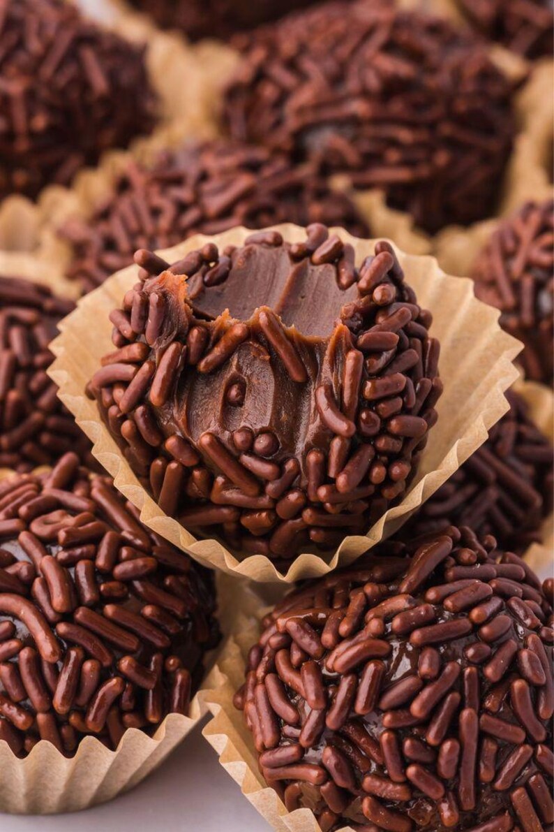 May include: Close-up of several chocolate truffles, each coated in chocolate sprinkles and nestled in a paper cup. One truffle has a bite taken out of it, revealing the soft, chocolatey interior. The truffles are a rich brown color.