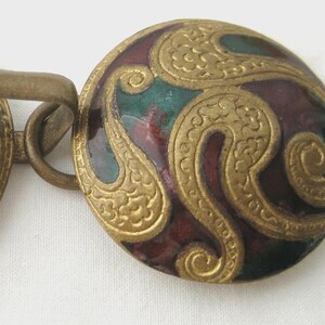 May include: Two-part clasp with a decorative design. Each circular piece features a gold-colored border and intricate gold-colored swirls on a background of burgundy and teal enamel. The clasp is connected by a metal bar.