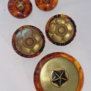 May include: A collection of vintage buttons in various designs. The buttons feature a tortoiseshell pattern with gold-colored metal accents. Some have a cross design, while others have floral or star motifs.