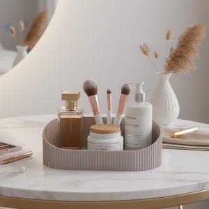 Puede incluir: Una mesa de tocador con tapa de mármol presenta una selección de productos de belleza. Una bandeja contiene brochas de maquillaje, perfume y productos para el cuidado de la piel. También hay una paleta de maquillaje, lápiz labial y espejo. Un jarrón con flores secas está en el fondo.