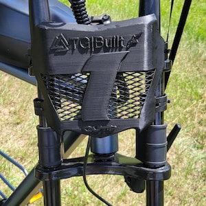 May include: A black 3D-printed front number plate for an electric bicycle, featuring the text ATG Built and a large number 1 embossed on the front. The plate has a mesh-like grid pattern and is mounted between the handlebars and the front fork.