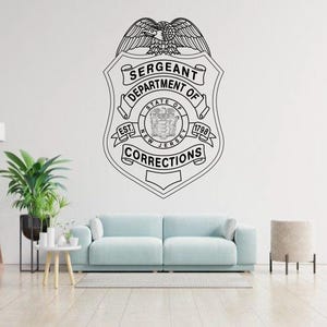 Op de afbeelding: Een zwarte lijntekening muursticker van een schildvormig embleem met een adelaar aan de bovenkant, met de tekst SERGEANT DEPARTMENT OF CORRECTIONS en STATE OF NEW JERSEY EST. 1798, gecentreerd op een witte muur boven een lichtblauwe bank.