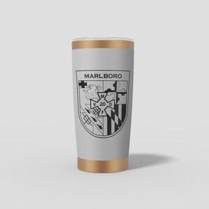May include: A light grey cylindrical tumbler with metallic gold rims at the top and bottom. The front features a black printed crest design with the text MARLBO RO above a shield containing various symbols and the central letters M, V, 20, D, F.