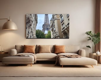 May include: A framed print of the Eiffel Tower in Paris hangs above a beige sectional sofa with orange and tan cushions. The room has a neutral colour palette with a floor lamp and a potted plant.