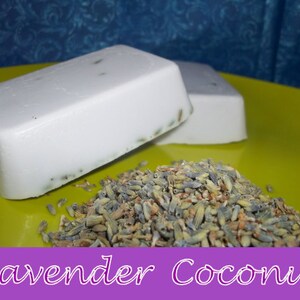 May include: Two bars of white soap with lavender buds embedded in the soap. The soap is on a yellow plate with dried lavender buds scattered around the soap.