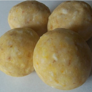 May include: Four round, yellow, and white, glazed, cake pops.