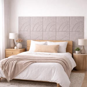 Op de afbeelding: Een slaapkamer met een bed met een licht houten hoofdbord en een neutraal gekleurd hoofdbordpaneel. Het bed is opgemaakt met wit beddengoed, een beige sprei en een bijpassend lendenkussen. Twee nachtkastjes met lampen en decoratie maken de scène compleet.