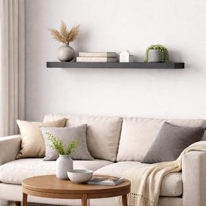 Può includere: Interno di un soggiorno con una mensola nera con decorazioni: un vaso con piante secche, libri, una casetta e una pianta in vaso. Sotto, un divano beige con cuscini e un tavolino rotondo in legno.