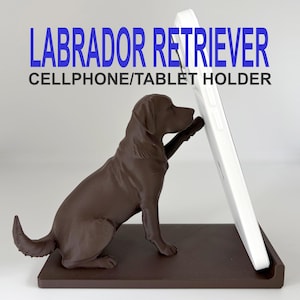 Peut inclure: Une figurine de Labrador Retriever marron servant de support pour téléphone portable ou tablette, avec le texte LABRADOR RETRIEVER CELLPHONE/TABLET HOLDER. Le chien est assis avec une patte étendue pour soutenir un appareil mobile blanc.