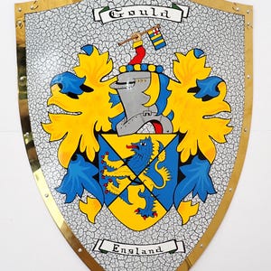 Może przedstawiać: Tarcza ze złotą obwódką i popękanym białym tłem. Tarcza przedstawia herb z hełmem, flagą oraz niebiesko-żółtym wzorem. U góry napis "Gould", a u dołu "England".
