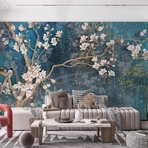May include: A living room with a teal floral mural featuring white blossoms and birds. A modern sofa, coffee table, and a red armchair are in front of the mural. A small tree in a pot is on the right.