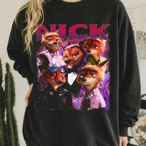 Op de afbeelding: Zwarte sweatshirt met een afbeelding van Nick Wilde uit Zootopia in verschillende outfits. Het woord "NICK" staat in roze en paars boven de afbeelding. Een casual, comfortabele stijl.