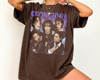 May include: A brown t-shirt with a graphic of a group of people and the word "SEONGHWA" in purple. The image is a portrait of five people. The t-shirt has short sleeves and a loose fit.