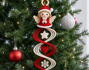 Op de afbeelding: Een gehaakte kerstversiering met een kleine engel in een rode muts en jurk, hangend aan een houten ring. Onder de engel bevindt zich een rood-crèmekleurige spiraalstructuur met een witte ster, een rood hart en een witte sneeuwvlok als versiering.