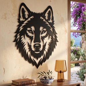 May include: A black metal wall art piece featuring a detailed, stylised wolf head silhouette with sharp, angular fur patterns and piercing eyes. The design is symmetrical, showcasing a bold, cutout aesthetic that highlights the wolf's facial features.
