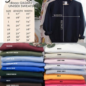 Op de afbeelding: Een marineblauw Gildan unisex sweatshirt hangt aan een houten hanger, met een maattabel en kleuropties. De tabel geeft maten S tot 5XL weer, met lengte- en breedtematen in cm. Kleuropties zijn onder meer bordeauxrood, zwart en wit.