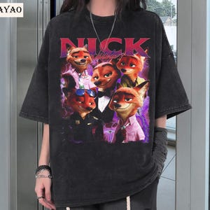 Op de afbeelding: Zwart T-shirt met een afbeelding van het personage Nick Wilde uit de animatiefilm Zootopia. De afbeelding toont Nick in verschillende poses met het woord "NICK" in rode letters. Het shirt heeft korte mouwen en een losse pasvorm.