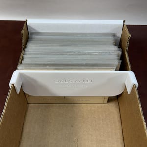 May include: Open cardboard box with a white plastic insert labeled "CARD STAY NET". The box contains a stack of clear, protective card sleeves. The box is brown and the insert is white.