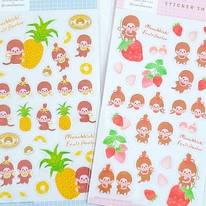 Puede incluir: Dos hojas de pegatinas transparentes con un personaje de mono de dibujos animados. La hoja de pegatinas de la izquierda tiene un tema de piña y la hoja de pegatinas de la derecha tiene un tema de fresa. Ambas hojas tienen el texto "Monchhichi Fruit Parlor" impreso en ellas.