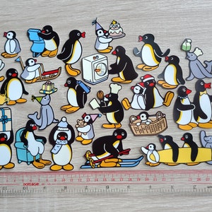 May include: A collection of cartoon penguin stickers in various poses and activities. The penguins are primarily black and white with yellow feet and beaks. Some penguins are holding gifts, wearing hats, or using skis. A ruler is placed at the bottom.