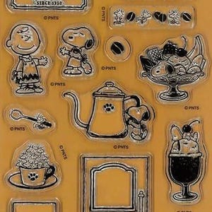 May include: Clear stamp set featuring Peanuts characters and coffee-themed images. Includes Snoopy, Charlie Brown, coffee cups, a coffee pot, and the words "Coffee House". The set contains 14 stamps.