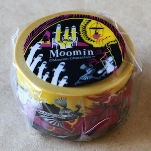 May include: A roll of decorative tape featuring Moomin characters. The tape has a yellow base with a repeating pattern of Moomin illustrations in black, white, and red. The top of the roll has a black and yellow label with the Moomin logo.