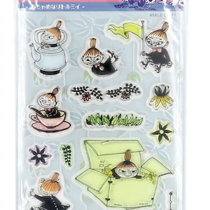 May include: A clear stamp set featuring Moomin characters, including Little My. The stamps are in a clear plastic sheet with the word "MOOMIN" at the top. The stamps include images of flowers, a teapot, and a box. The text "ひょっこりクリアスタンプ" is also visible.