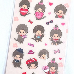 以下が含まれることがあります： 人気アニメキャラクターのモンチッチの様々なイラストが描かれたステッカーシート。ステッカーは透明な背景にピンクのハートと花が描かれている。ステッカーには、ハートを持っているモンチッチ、帽子をかぶっているモンチッチ、お茶を飲んでいるモンチッチなど、様々なポーズのモンチッチが描かれている。シートの上部には「モンチッチステッカー」という文字が印刷されている。