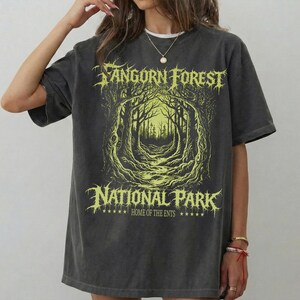 Op de afbeelding: Donkergrijze t-shirt met een distressed grafisch ontwerp. Het ontwerp toont de tekst "Fangorn Forest National Park" in een gestileerd lettertype, met een gele illustratie van een boslandschap. Het shirt heeft een relaxte pasvorm.