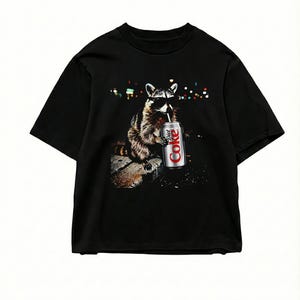 May include: Black t-shirt featuring a raccoon wearing sunglasses and drinking from a Diet Coke can. The raccoon is depicted in a photorealistic style against a blurred background of city lights. The Diet Coke can is silver and red.