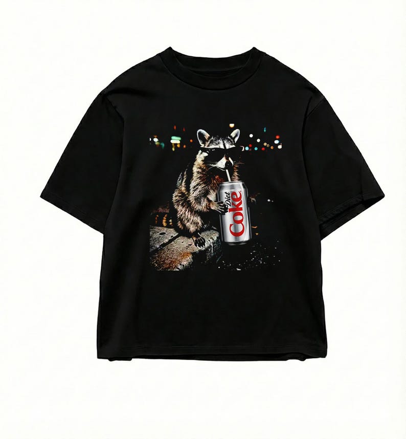 May include: Black t-shirt featuring a raccoon wearing sunglasses and drinking from a Diet Coke can. The raccoon is depicted in a photorealistic style against a blurred background of city lights. The Diet Coke can is silver and red.