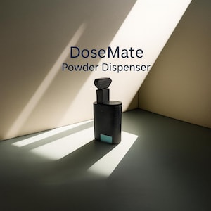 May include: A black powder dispenser with a geometric design, featuring a rectangular base and a stacked top. The dispenser has a small, light blue accent and the text "DoseMate Powder Dispenser" in blue.
