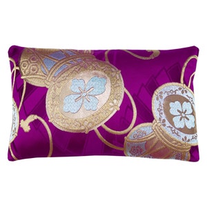 Puede incluir: Un cojín rectangular decorativo con un vibrante fondo magenta. El cojín presenta un diseño ornamentado de formas circulares y ovaladas doradas y plateadas con motivos florales. El diseño está bordado en el cojín.