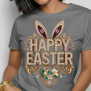 May include: A grey t-shirt with a decorative Easter design. The design features jeweled bunny ears with purple gems, the words "HAPPY EASTER" in jeweled letters, and a basket with flowers and a bunny. The t-shirt has short sleeves.