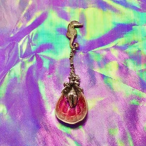May include: A decorative metal spoon featuring a seahorse handle and a bowl shaped like a seashell. The interior of the seashell bowl is painted in a vibrant magenta pink, while the exterior and handle have a metallic silver finish.