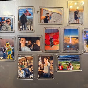 Könnte beinhalten: Eine Sammlung gerahmter Fotografien, jeweils in transparenten Acrylgehäusen. Die Bilder zeigen verschiedene Szenen, darunter Menschen, Landschaften und Ereignisse. Die Rahmen sind auf einer metallischen Oberfläche befestigt.