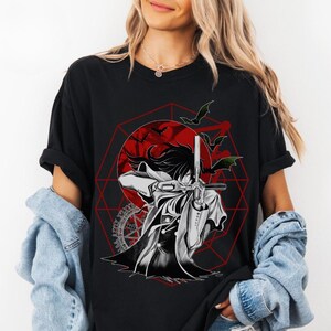 May include: Black t-shirt featuring a graphic of an anime character with a sword, set against a red geometric design and a red sun. Bats are flying in the background. The design is in black, white, and red.