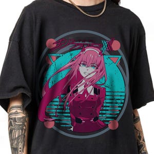 May include: Dark gray t-shirt featuring an anime-style illustration of a female character with pink hair and blue eyes. The design includes Japanese text and a teal and pink graphic.