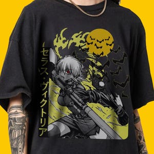 May include: Black t-shirt featuring a manga-style illustration of a female character with a weapon, set against a yellow backdrop with a full moon and bats. Japanese text is visible on the left side of the graphic.