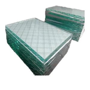 Könnte beinhalten: Zwei Stapel quadratischer Glasscheiben mit einem auf der Oberfläche geätzten Gittermuster. Das Glas hat einen leichten Grünstich an den Kanten. Die Quadrate sind ordentlich gestapelt und bilden eine geometrische Darstellung.