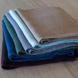 May include: A stack of folded linen napkins in various colors, including brown, blue, green, and purple. The napkins are arranged in a layered fashion, showcasing their different hues and textures. The fabric appears to be woven, with a slightly textured surface.
