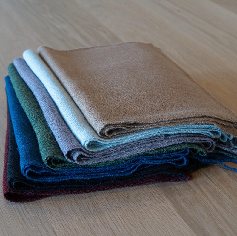 May include: A stack of folded linen napkins in various colors, including brown, blue, green, and purple. The napkins are arranged in a layered fashion, showcasing their different hues and textures. The fabric appears to be woven, with a slightly textured surface.
