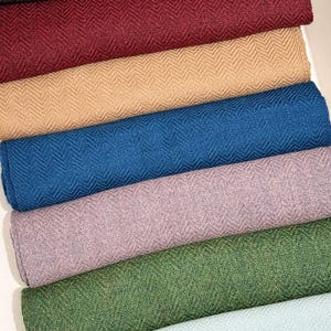 May include: A collection of folded fabric rolls in various colors, including black, burgundy, tan, blue, lavender, green, and light blue. Each roll displays a textured herringbone pattern, suggesting a woven textile material.