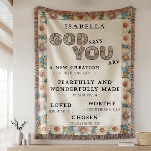May include: A beige tapestry with floral and geometric borders, featuring the text "ISABELLA GOD SAYS YOU ARE" and Bible verses. The tapestry is displayed on a wooden shelf with decorative items.