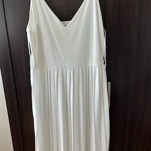 May include: A white midi dress with a V-neckline and spaghetti straps. The dress features a pleated skirt and a simple, elegant design. The dress is made of a lightweight fabric.
