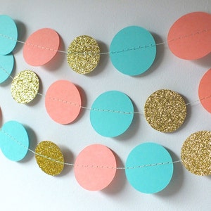 May include: A garland made of paper circles in coral, turquoise, and gold glitter. The circles are strung together with white thread.