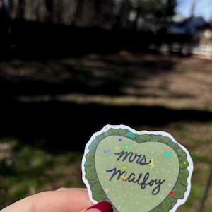Channel your Slytherin romance era with this “Mrs. Malfoy” inspired sticker, perfect for fans of Draco Malfoy and the world of Harry Potter 🐍✨
This heart-shaped sticker features a soft green design with holographic sparkle details and is laminated for durability, making it perfect for water bottles, Kindle cases, laptops, journals, and planners. A must-have for bookish girlies and wizarding romance lovers.
✨ Fan-made, inspired design.