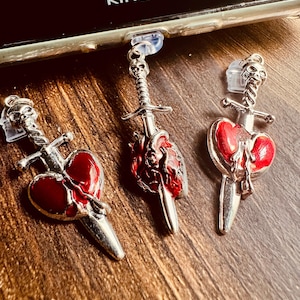 May include: Three silver-toned charms with red heart and sword designs. Each charm features a skull at the top. The charms are attached to clear plastic pieces. The word "kindle" is visible in the background.