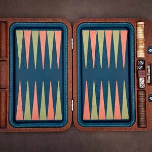 Könnte beinhalten: Ein Backgammon-Spiel aus Holz mit einem dunkelbraunen Rahmen und einer blauen Spielfläche. Das Brett zeigt abwechselnd hellgrüne und korallenfarbene Dreiecke. Enthalten sind zwei Stapel Holzspielsteine, zwei Paar Würfel und ein Verdopplungswürfel.