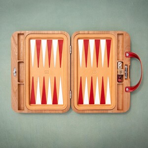 Könnte beinhalten: Ein hölzernes Backgammon-Spiel in einem offenen Koffer mit beigefarbenem Innenraum und roten sowie weißen dreieckigen Feldern. Das Set verfügt über einen roten Ledergriff, Metallverschlüsse und Würfel in den seitlichen Fächern des Rahmens.